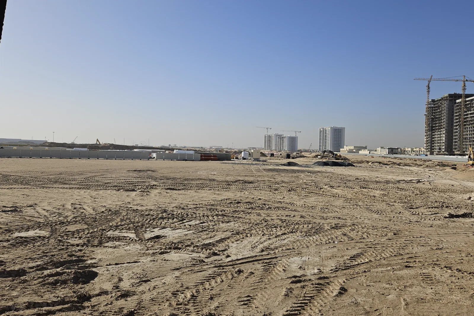 Propsearch January 2026 construction photo for Nura at the Wilds — empty graded sand behind hoarding, cranes on neighbouring plots